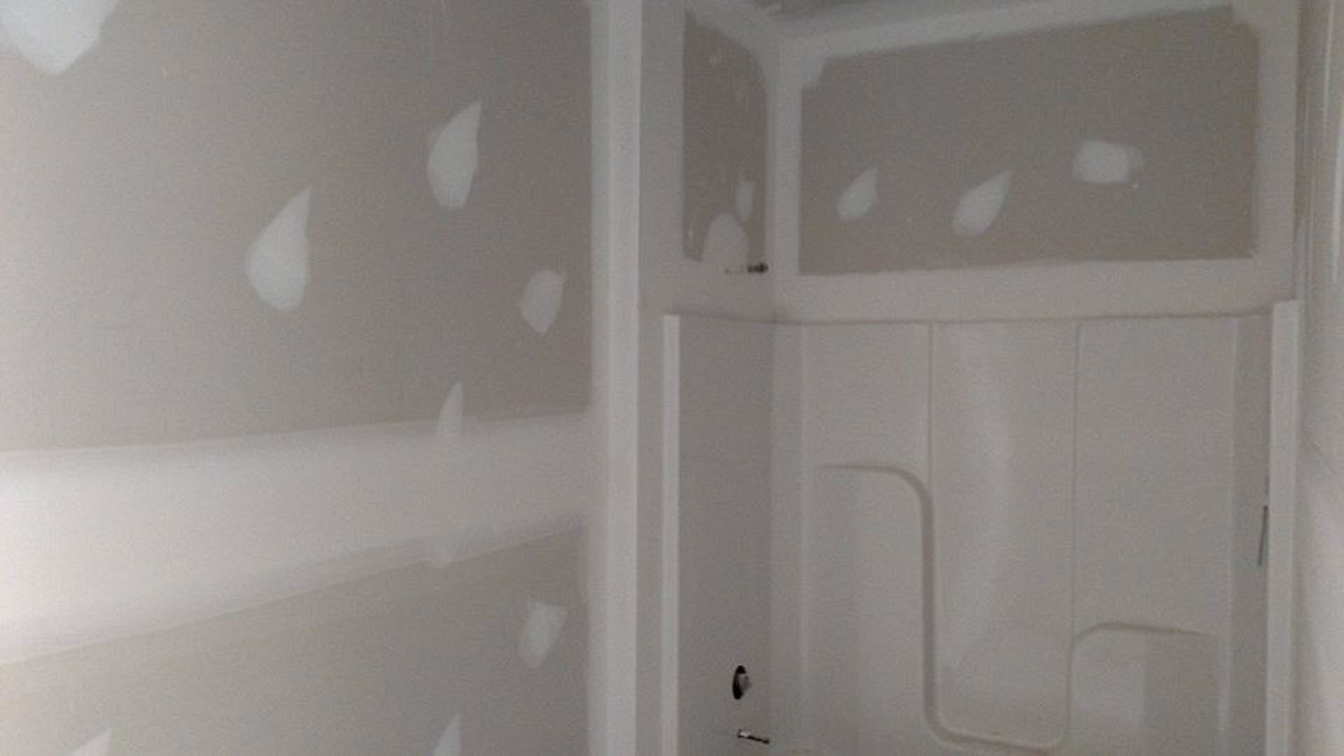 Bathroom with white plaster walls, white bathtub featuring a white handle, white toilet seat, and white countertop with subtle lines and a small black spot; white object rests on