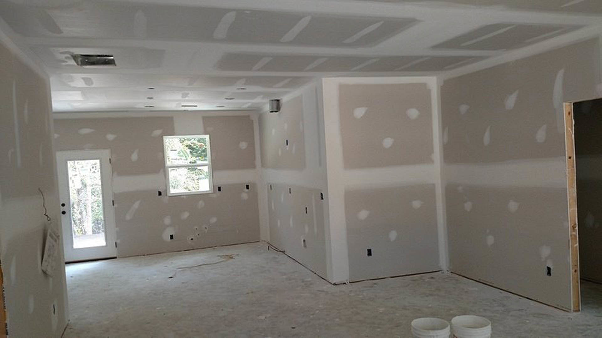 White-walled room with a concrete floor, white framed window, white door with glass panel, and several stacked white buckets