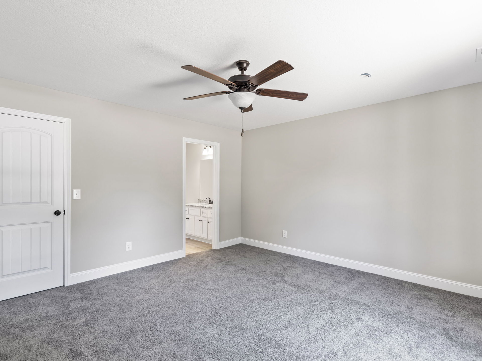 Ceiling fan with light fixture mounted above grey carpeted floor, white door, and neutral walls in a residential room
