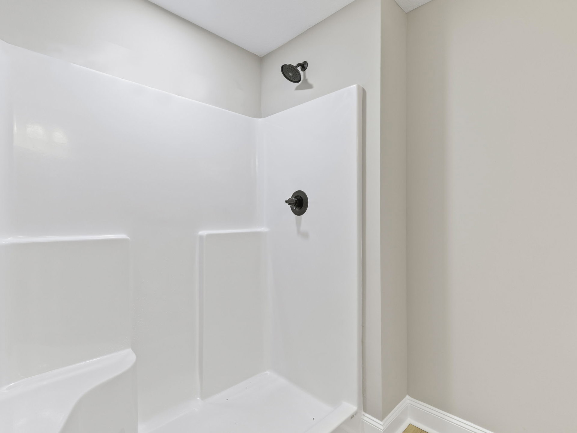 White tile shower with black framed glass door, round black showerhead, and built-in white bathtub.