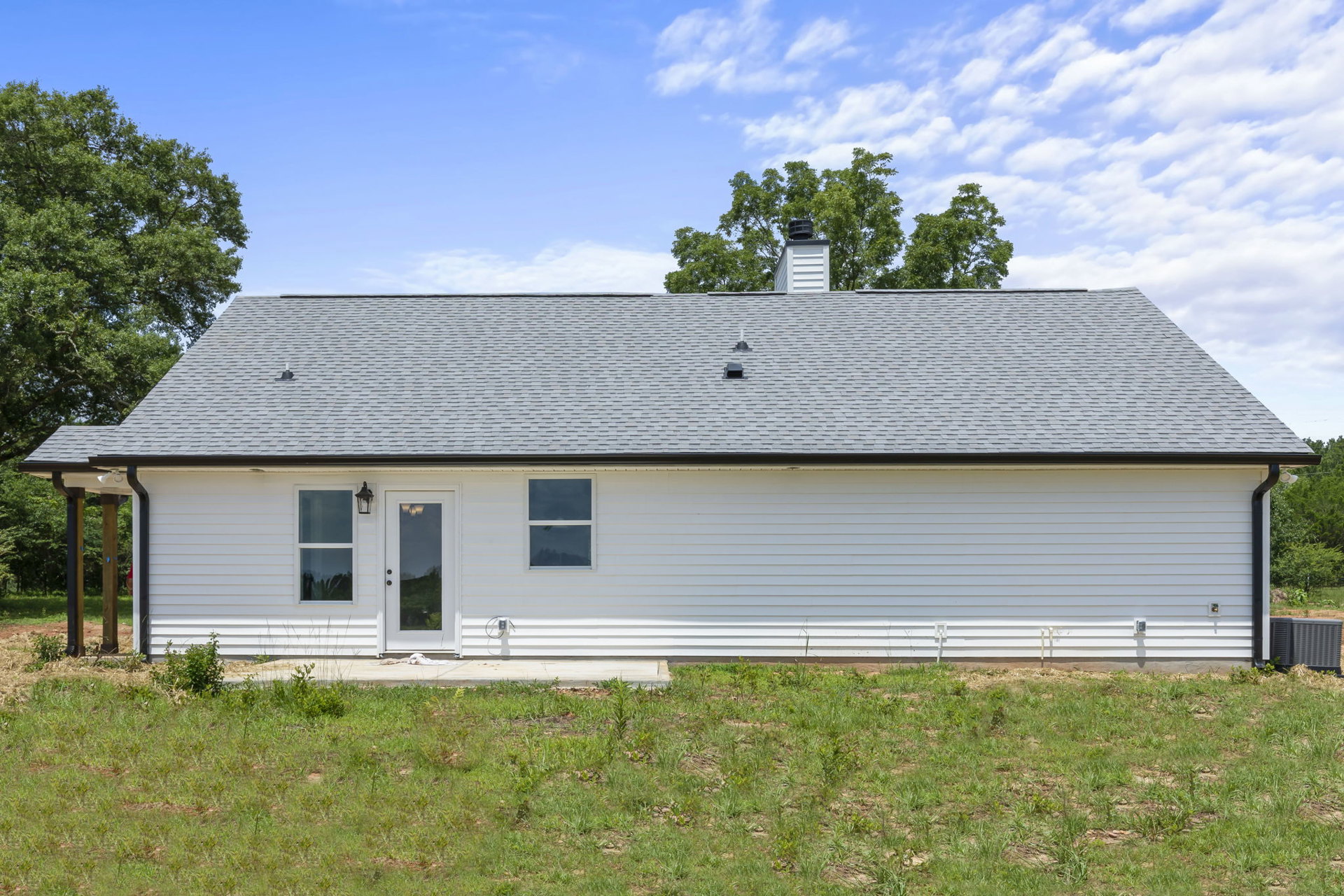 White siding home with glass panel door, white framed window, green lawn, mature trees, and cloudy sky in background