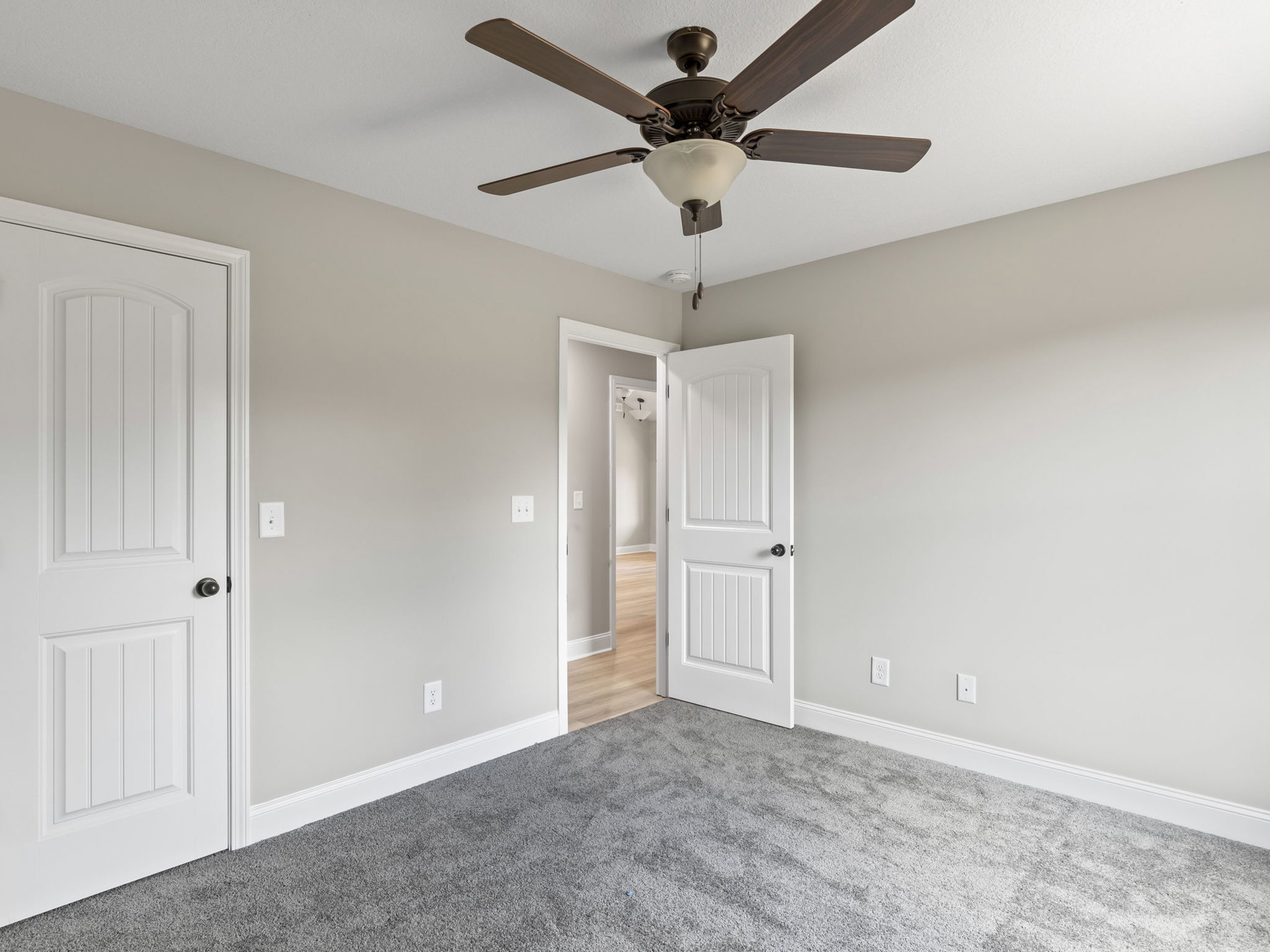 Ceiling fan with integrated light fixture, white paneled door with black knob, grey carpet flooring, white walls with crown molding