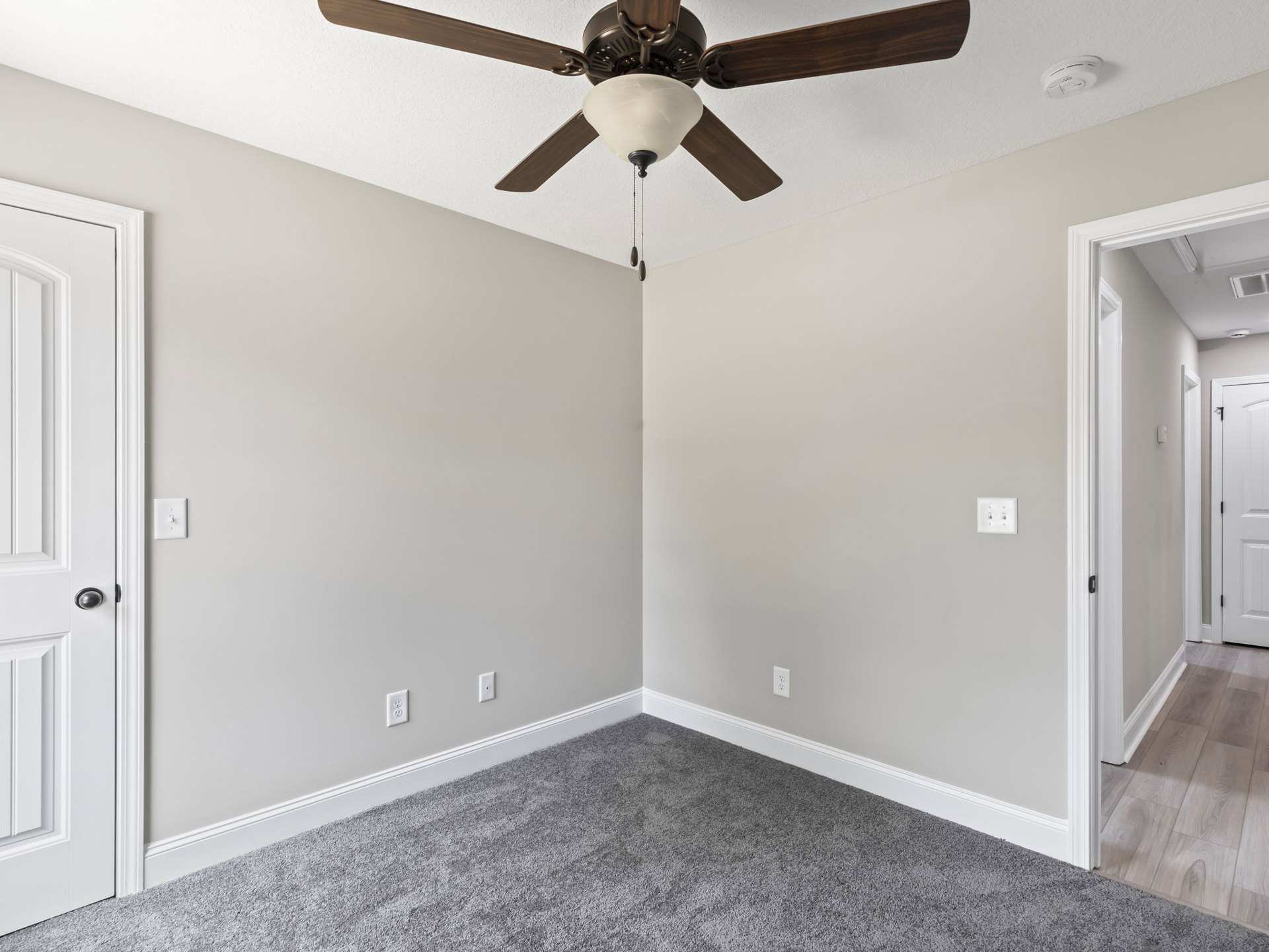 Ceiling fan with integrated light fixture mounted on white plaster ceiling above wood flooring, white door with black handle and two wall switches visible