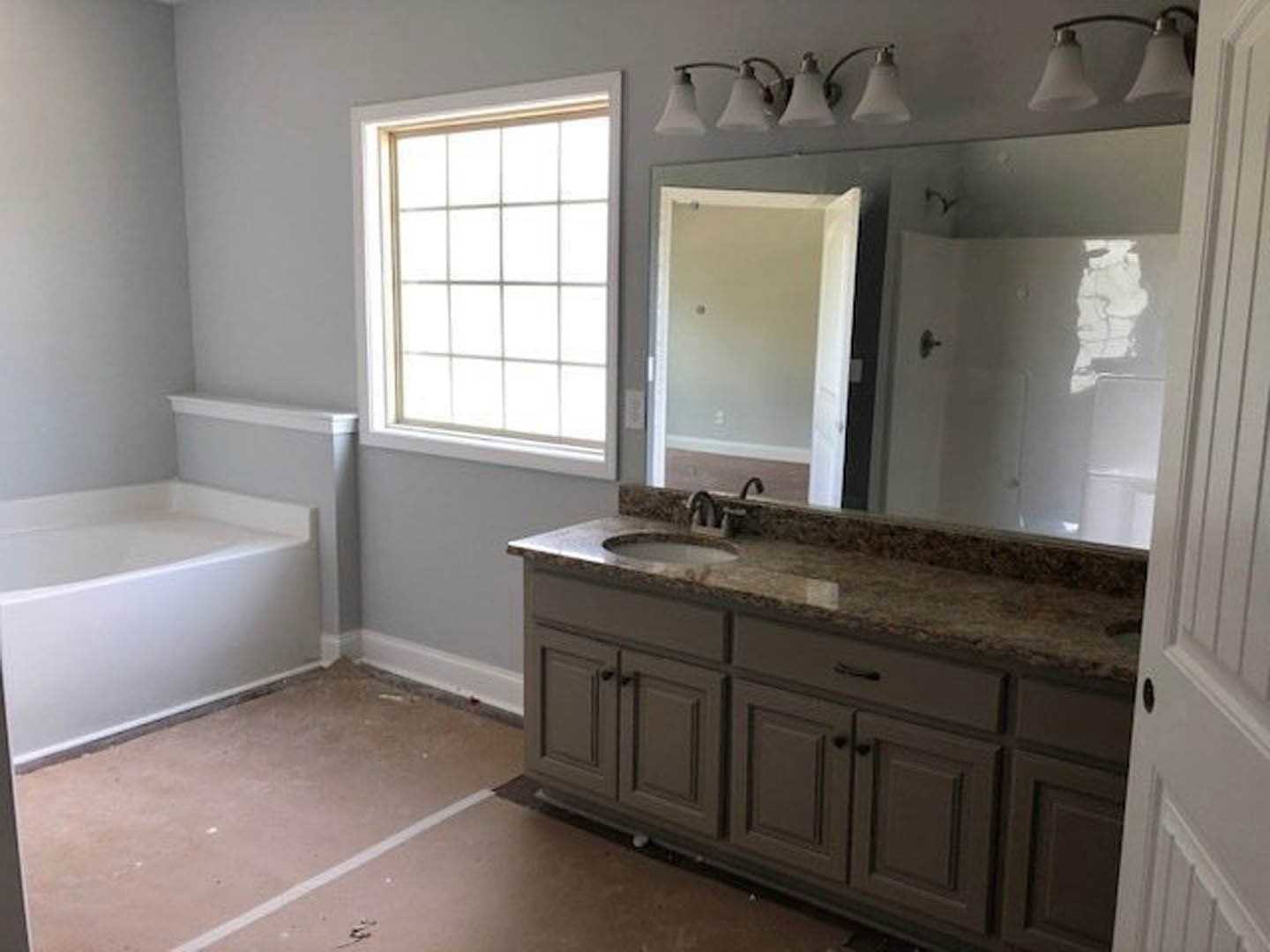 Bathroom with freestanding tub, expansive wall mirror, marble countertop vanity, tiled floor, and grid-style window.