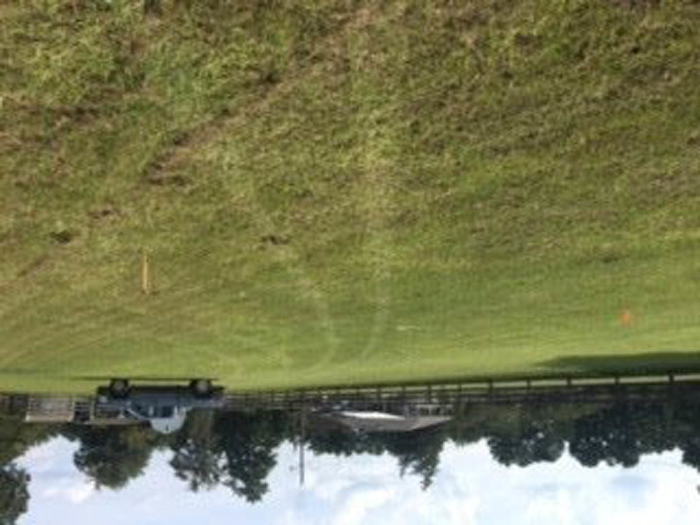Modern farmhouse exterior with white siding, black-framed windows, and a manicured green lawn bordered by a gravel driveway; pickup truck parked near the entrance.
