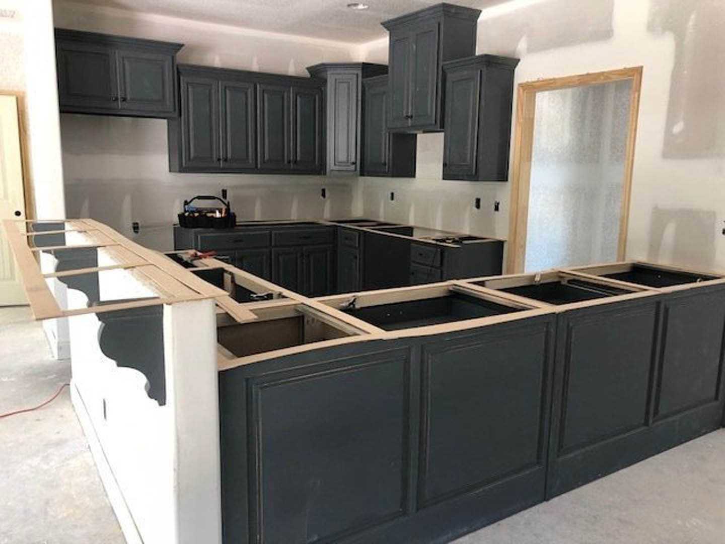 Black kitchen cabinets with wood trim, white countertops, tile backsplash, stainless steel sink, and modern appliances.