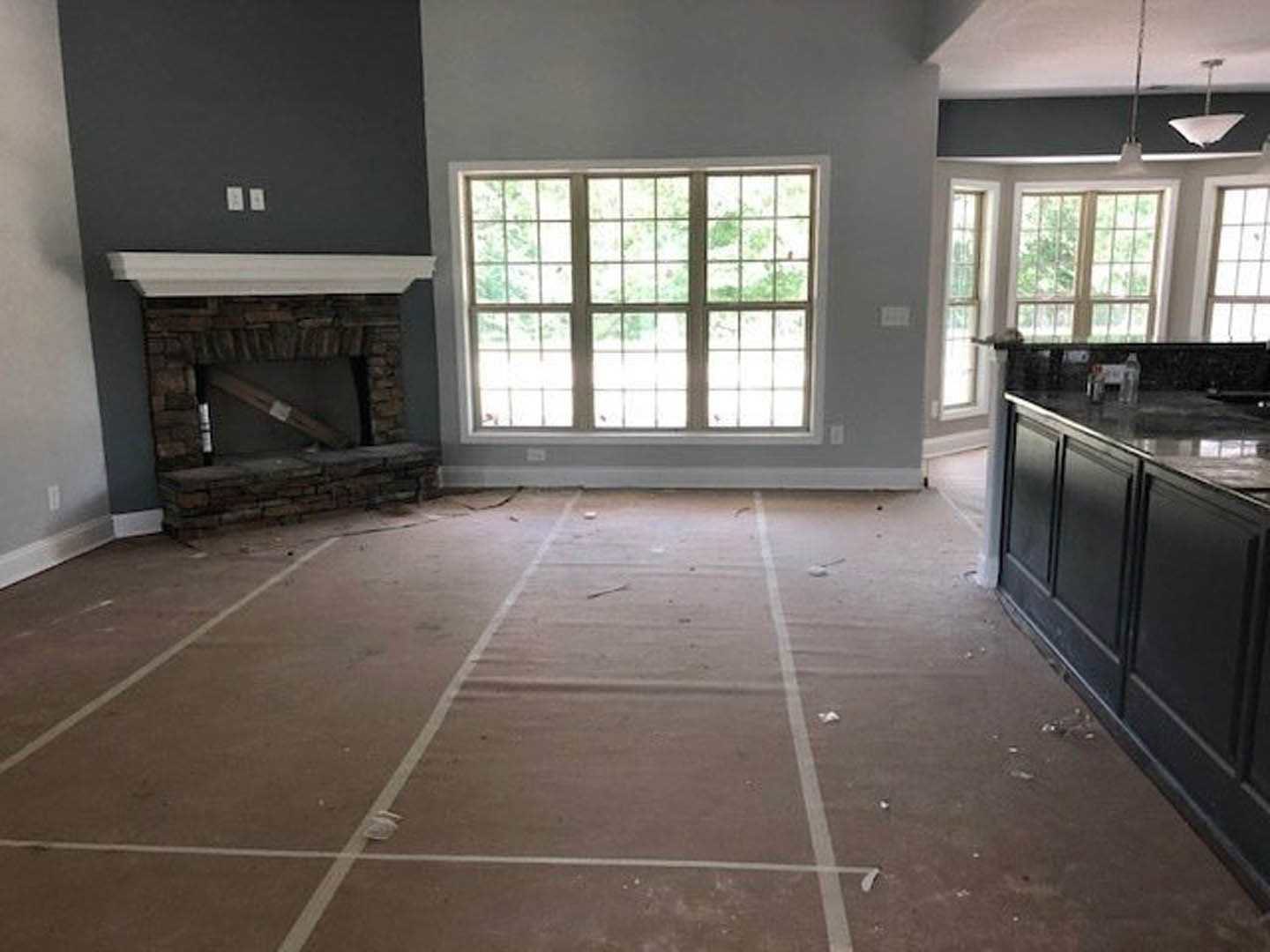 Open concept kitchen and living area featuring tile flooring, brick fireplace with wooden mantel, stainless steel stove, white cabinetry, stone countertops, and large windows.