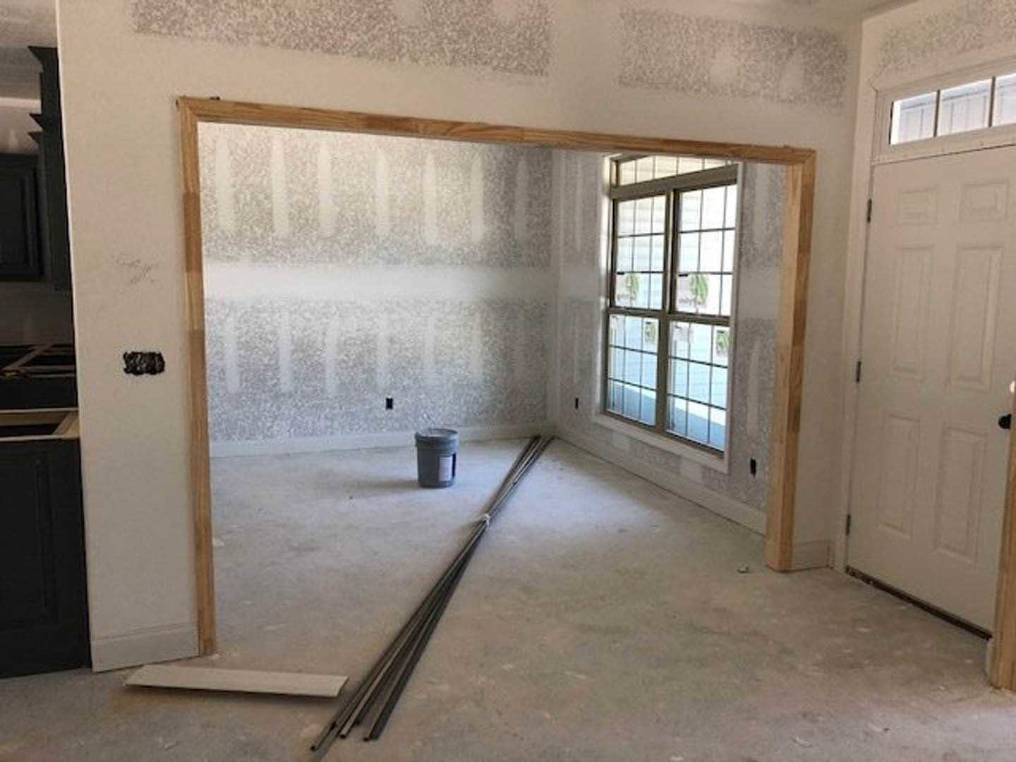 Light-filled room with white plaster walls, grey bucket of metal pipes on wood flooring, large window with black trim, white door with black knobs
