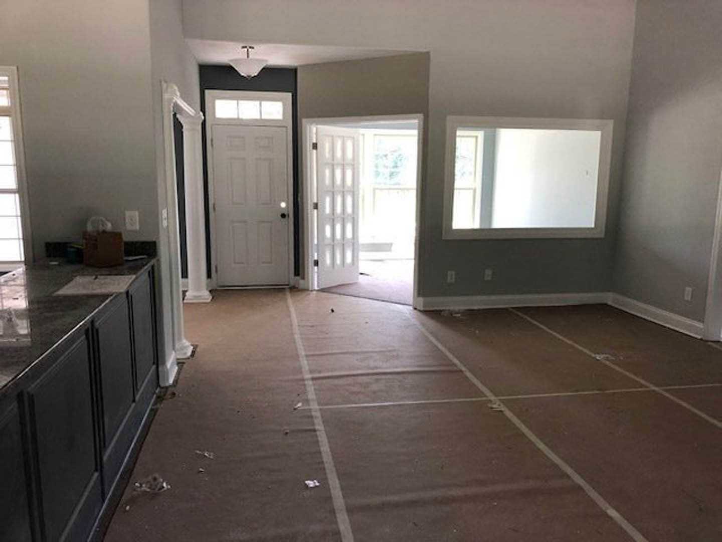 Tile-floored bathroom with a white sink, rectangular mirror, open white door with black handle, and person standing near a window.