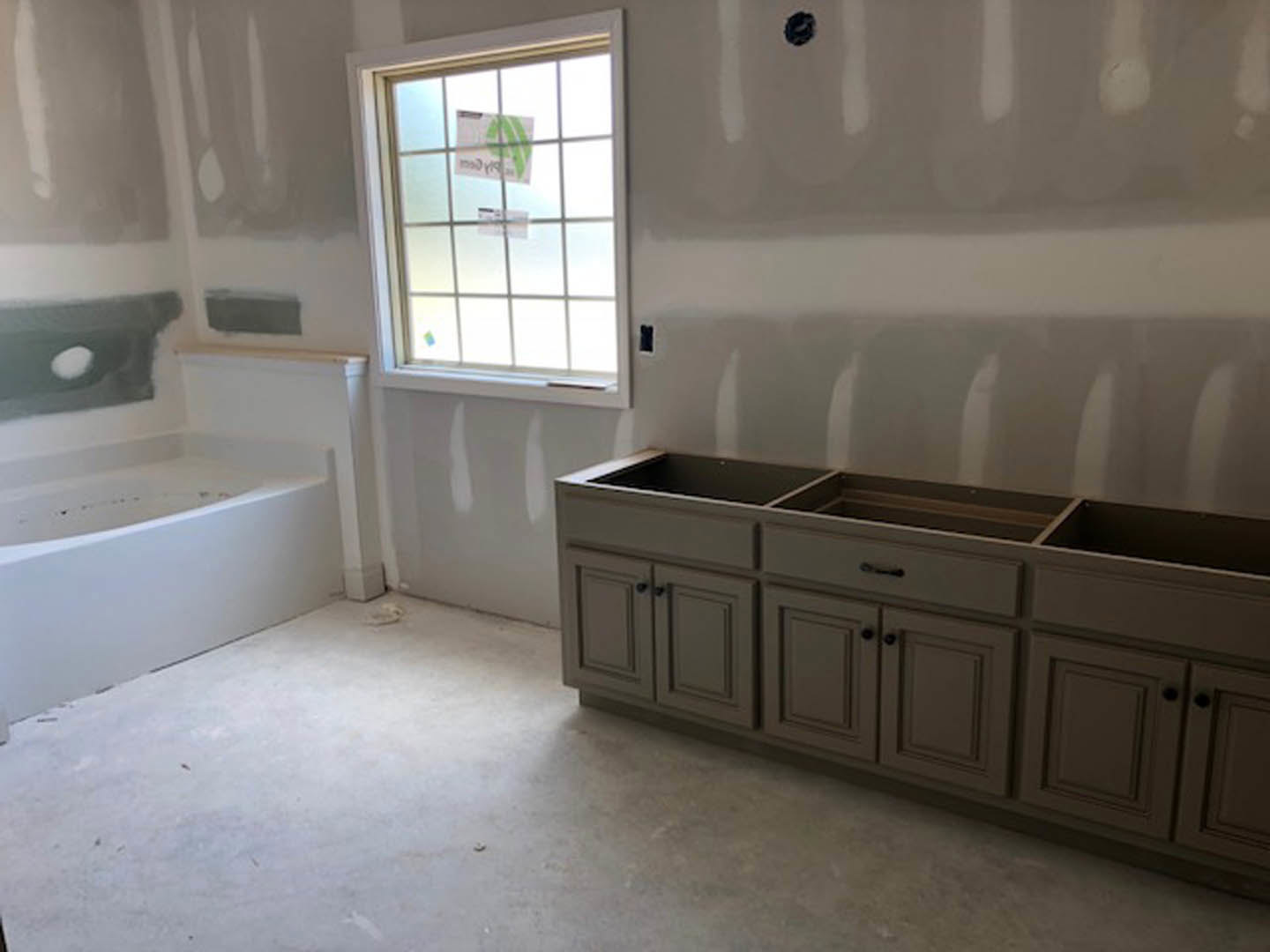 Bathroom with white freestanding bathtub, wood cabinets, tile flooring, and large window with sticker