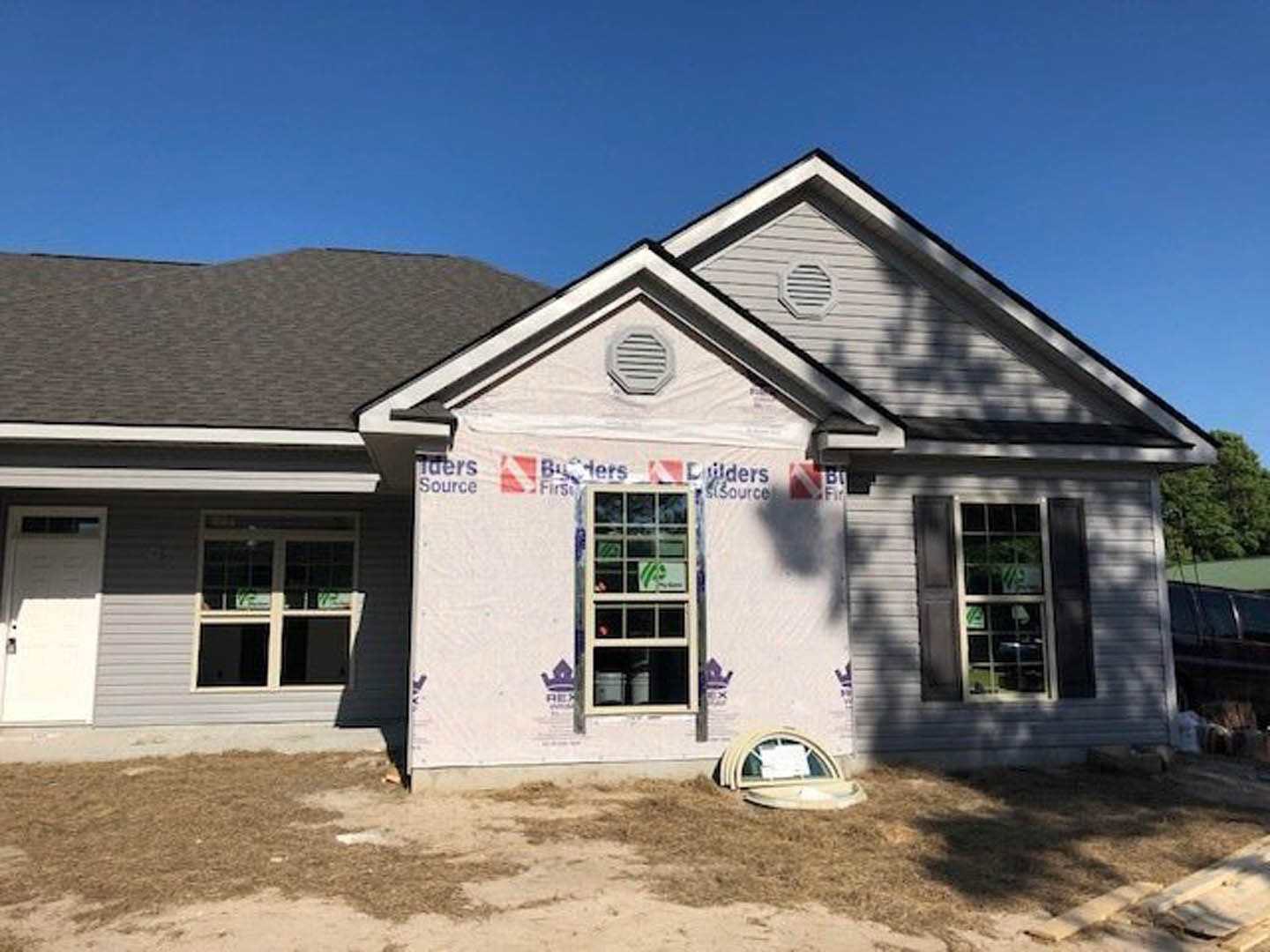 White exterior wall with multi-pane window, black-striped vent, and construction materials visible under clear blue sky