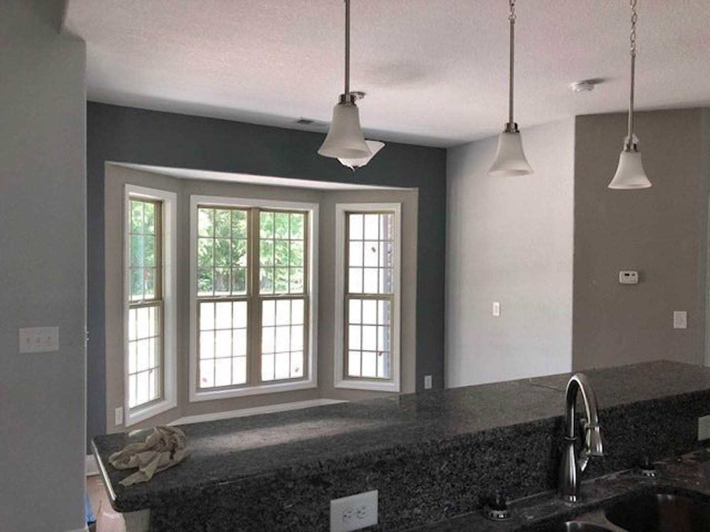 Bright kitchen featuring white cabinetry, stainless steel sink beneath large windows with blinds, marble countertops, and chrome faucet.