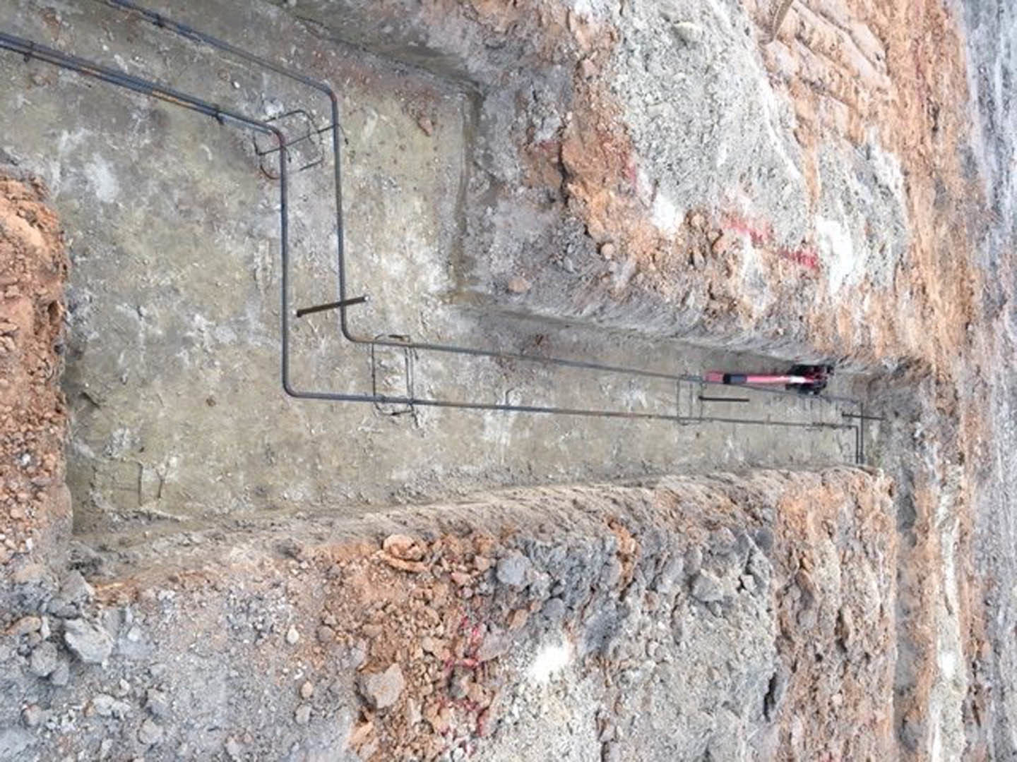 PVC pipe laid in a dirt trench beside a concrete foundation wall with limestone rocks scattered on the ground
