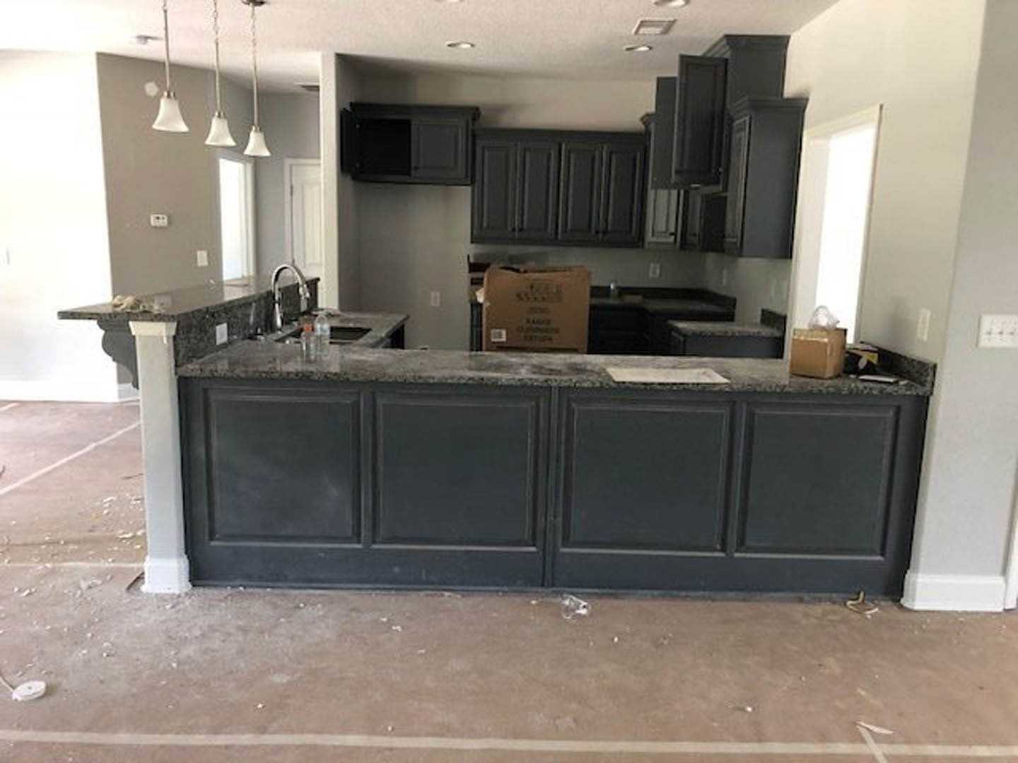 Modern kitchen with light stone countertop, white cabinetry, stainless steel sink, and built-in appliances; cardboard box with black text sits on the counter, pendant lights hang