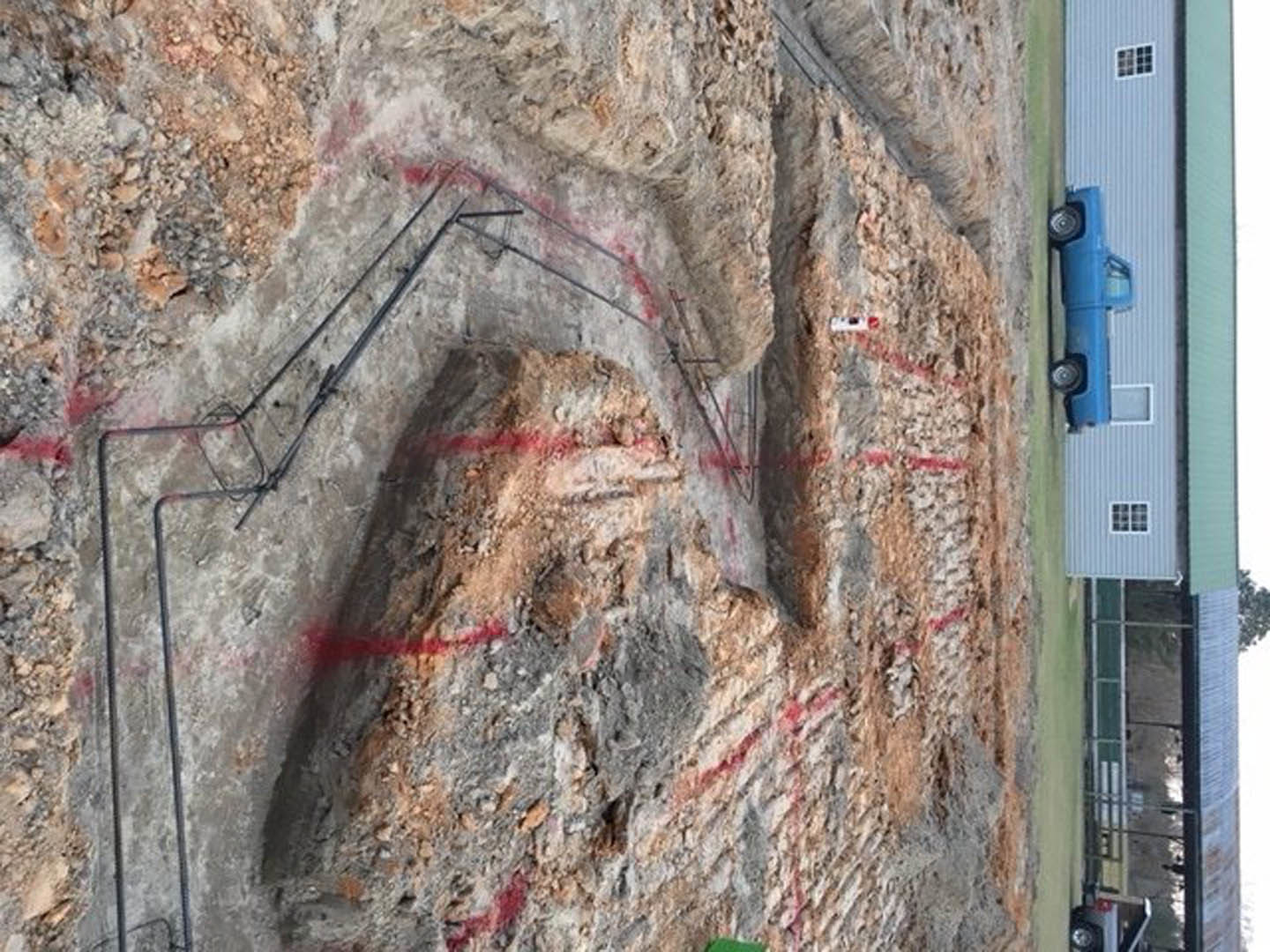 Blue pickup truck parked in driveway of modern home with white exterior, large grid windows, visible construction materials including pipes and gas can near entrance.