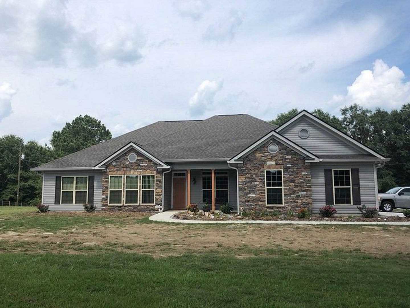 Two-story house with stone and siding exterior, white-framed windows, covered porch, manicured lawn, silver truck parked beside driveway, blue sky with scattered clouds