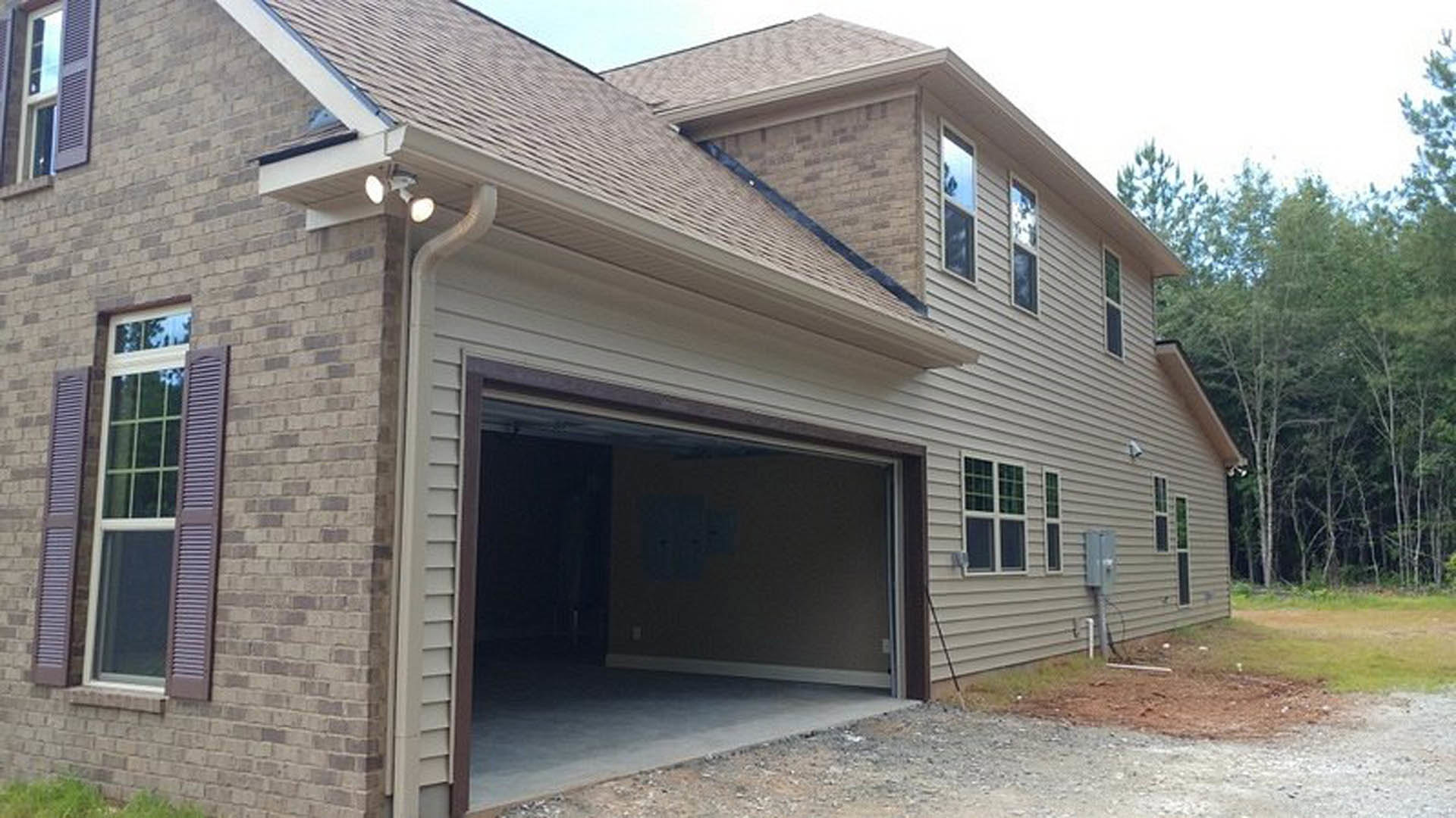 Open garage door revealing concrete floor, adjacent brick wall, and window with shutters on residential home exterior