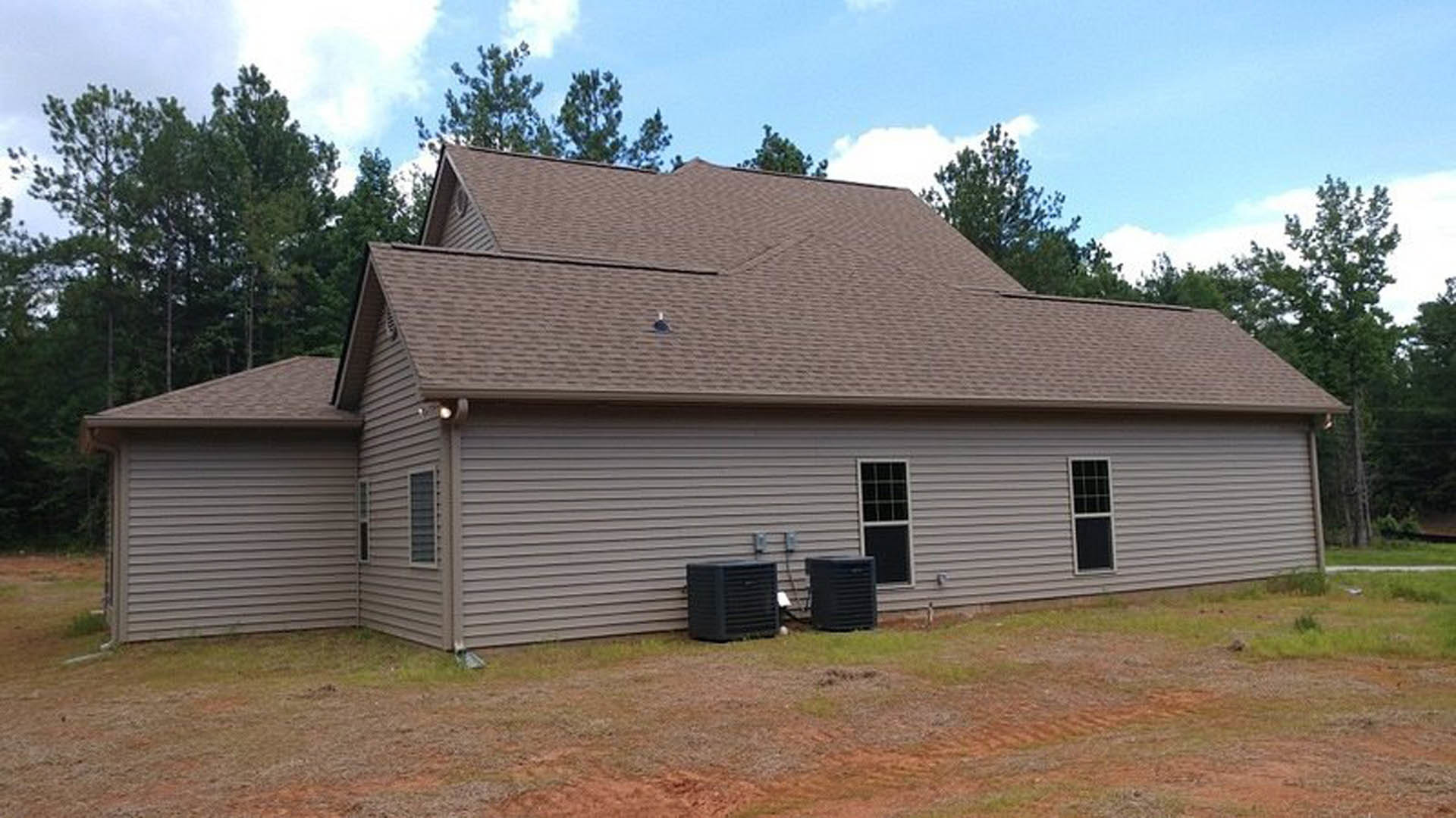 Modern house with white walls and large black box-shaped addition, expansive grassy yard, dirt patch in front, mature trees, cloudy sky.