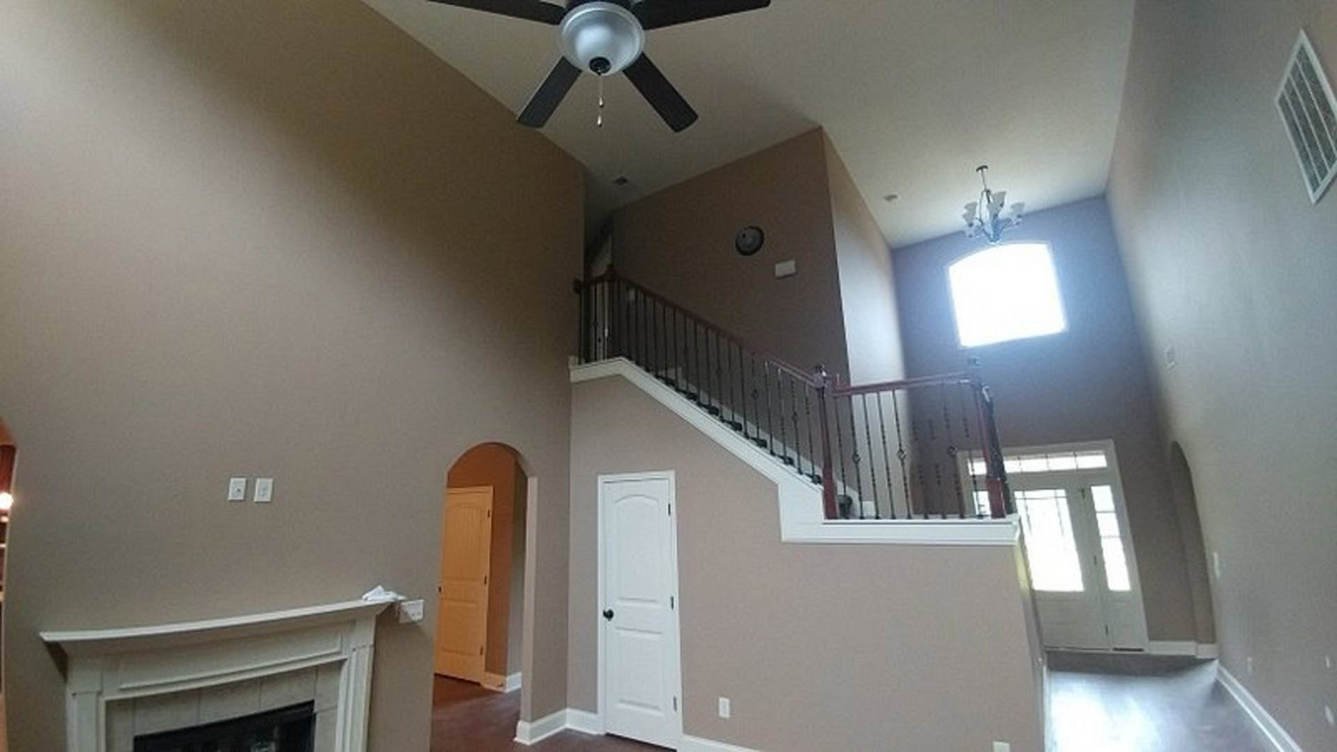 Wood staircase with white risers and dark handrail, adjacent to living area featuring a stone fireplace, crown molding, ceiling fan, and light plaster walls