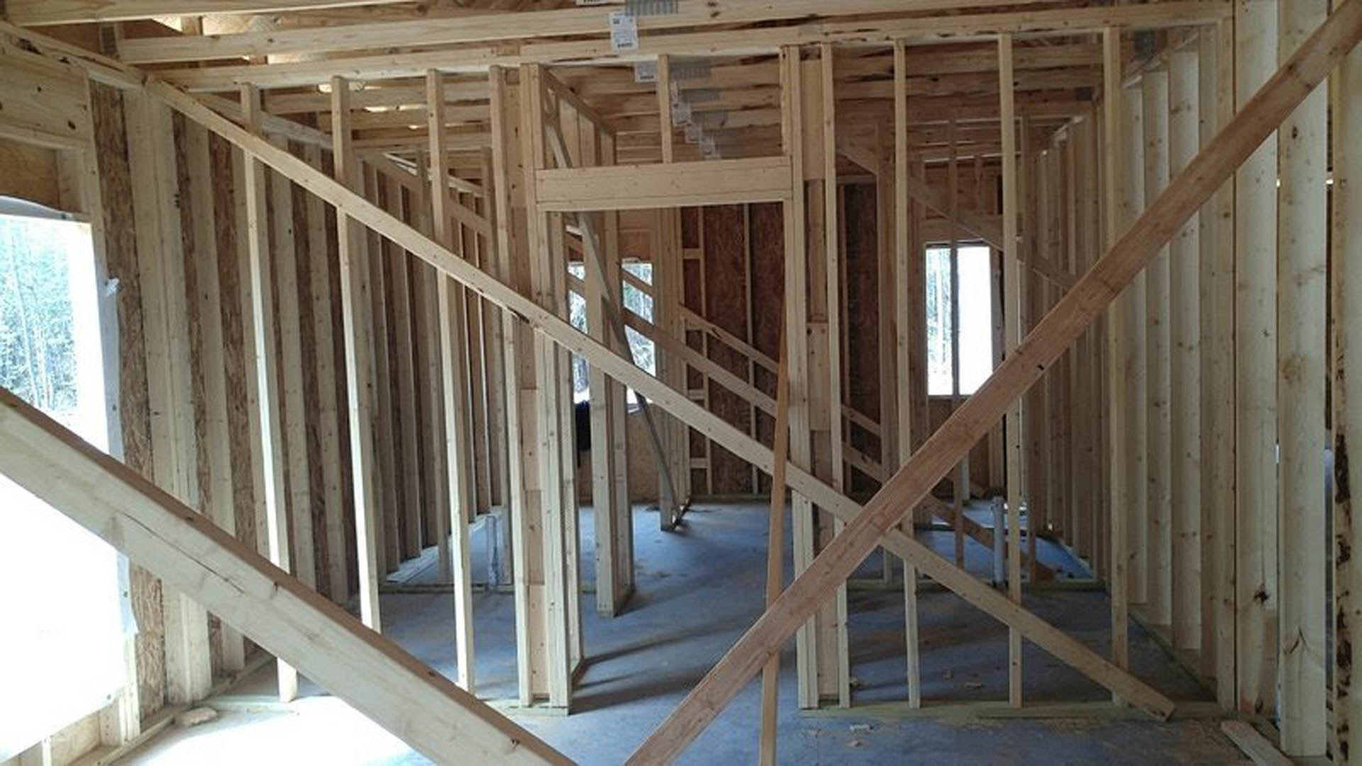 Exposed wooden beams and framing inside a partially constructed room, with a white sign featuring black text and a window visible in the background.