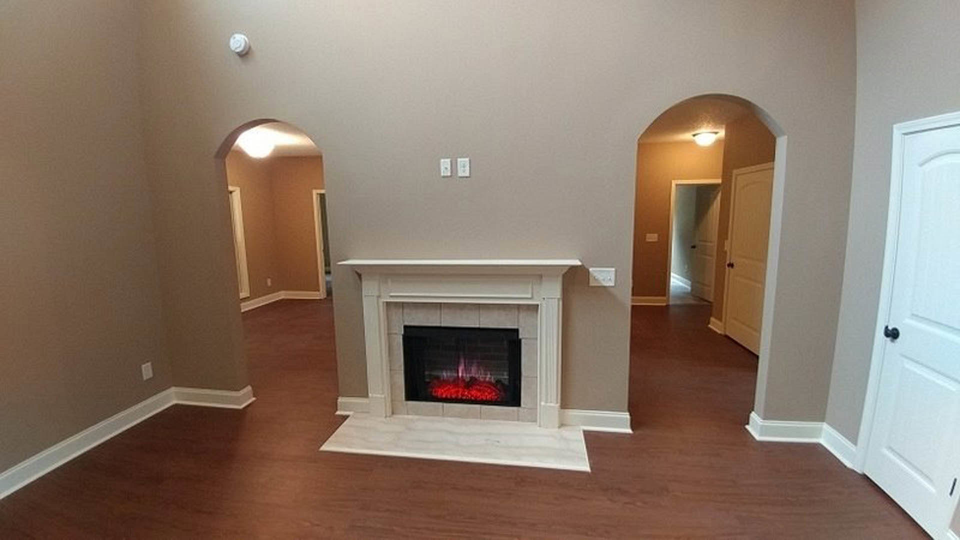 Stone fireplace with burning fire, white circular wall decor above mantel, freestanding bathtub with white towel, hardwood flooring, crown molding, and neutral painted walls