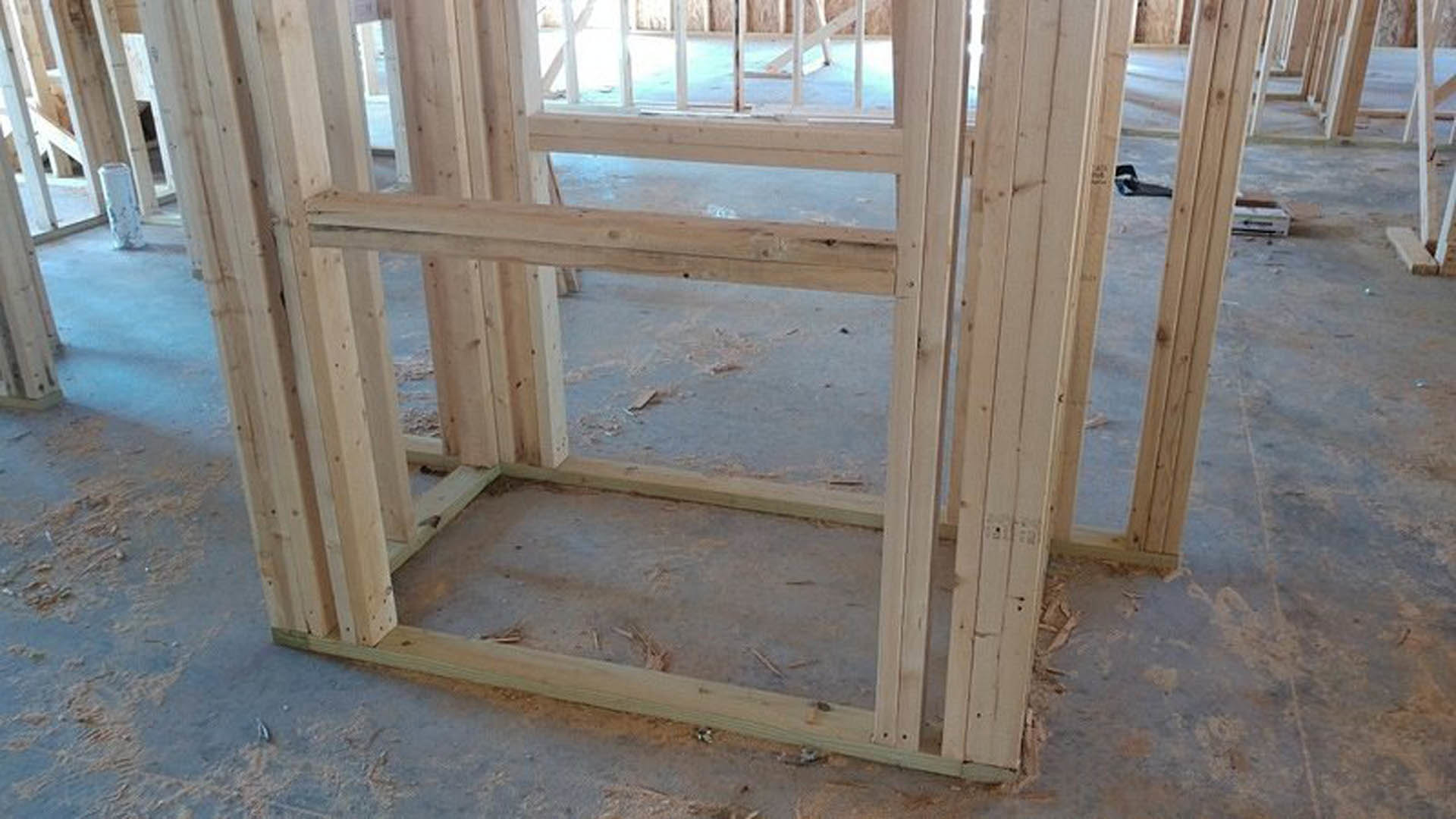 Exposed wood framing and lumber planks forming the structure of a custom home under construction, set on a concrete foundation indoors