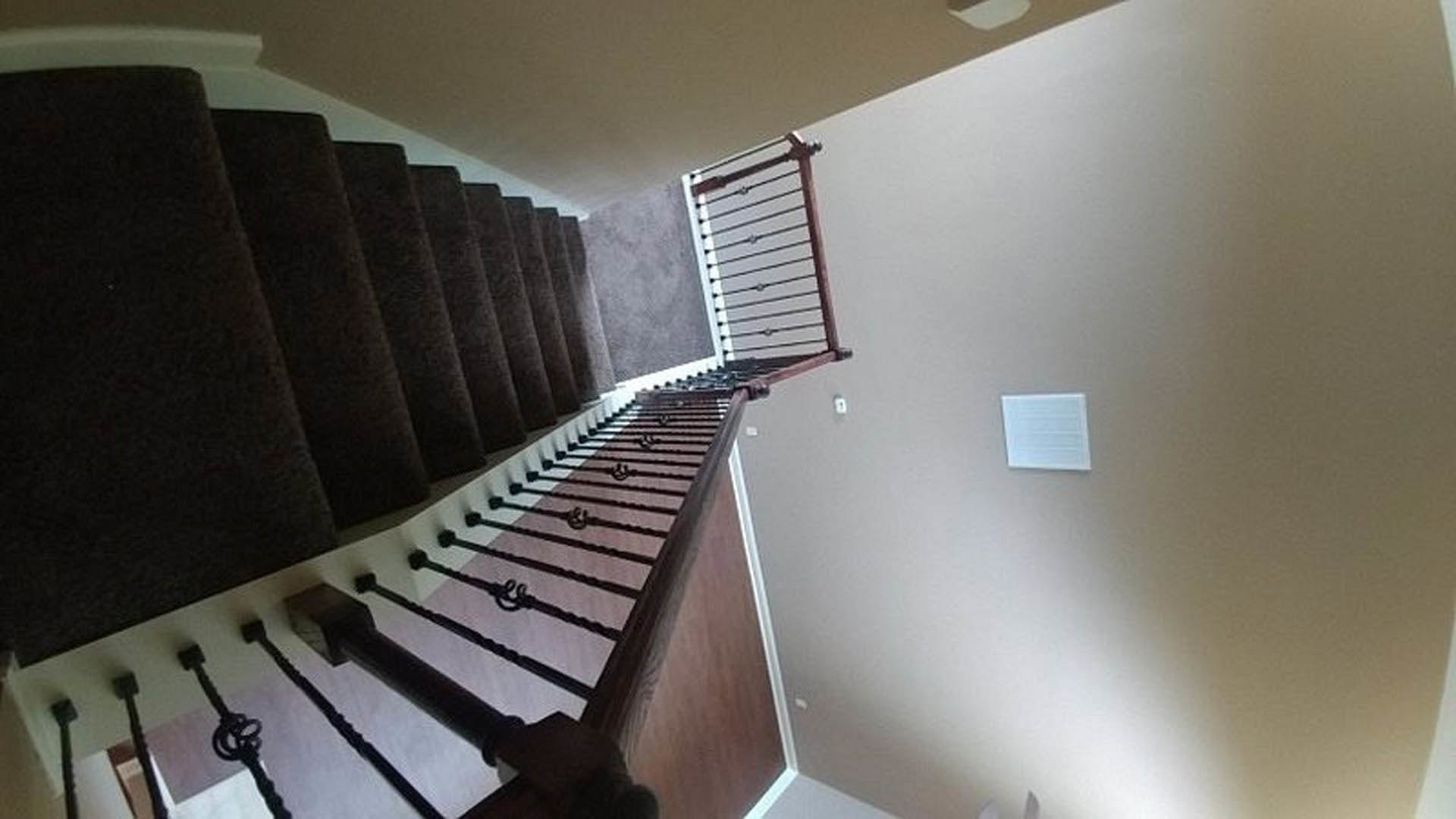 Staircase with brown carpeted steps, metal railing, and white walls in a residential interior