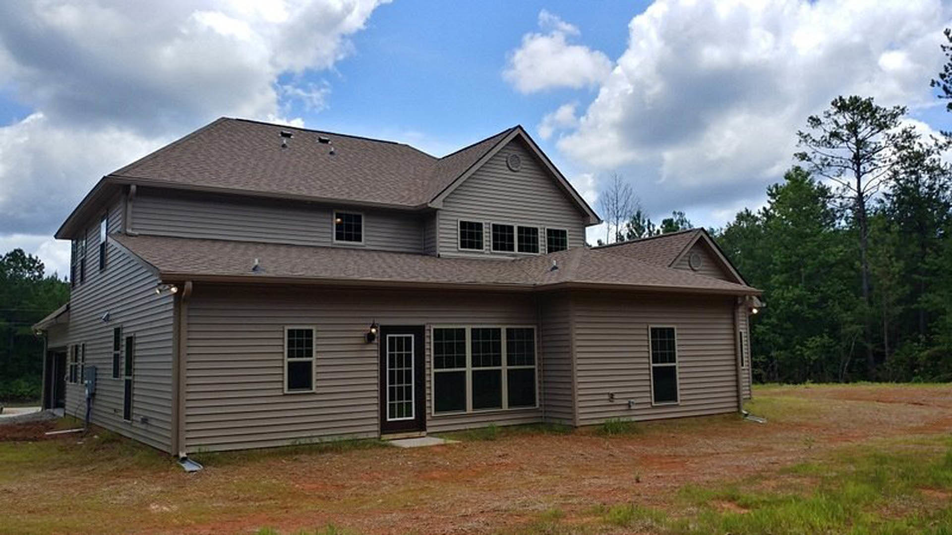 Two-story home with light siding, large front door, multiple white-framed windows, grassy yard, and mature trees in the background