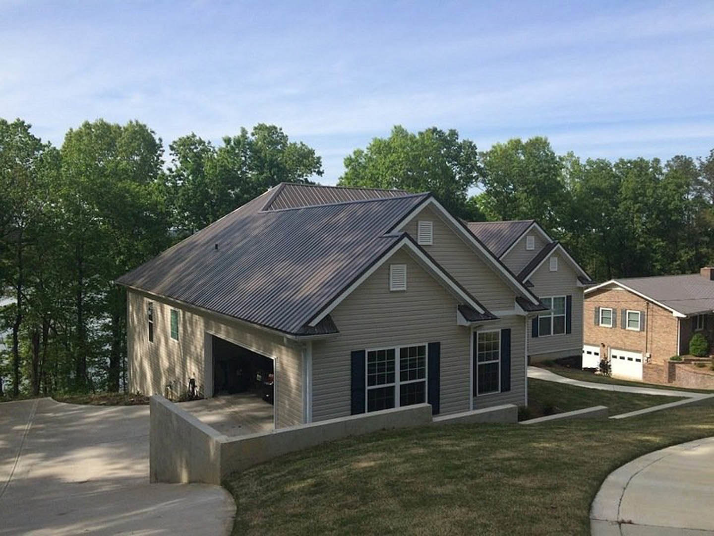 Two-story home with white siding, multi-pane windows, attached garage, paved driveway, gabled roof, and mature trees under a partly cloudy blue sky
