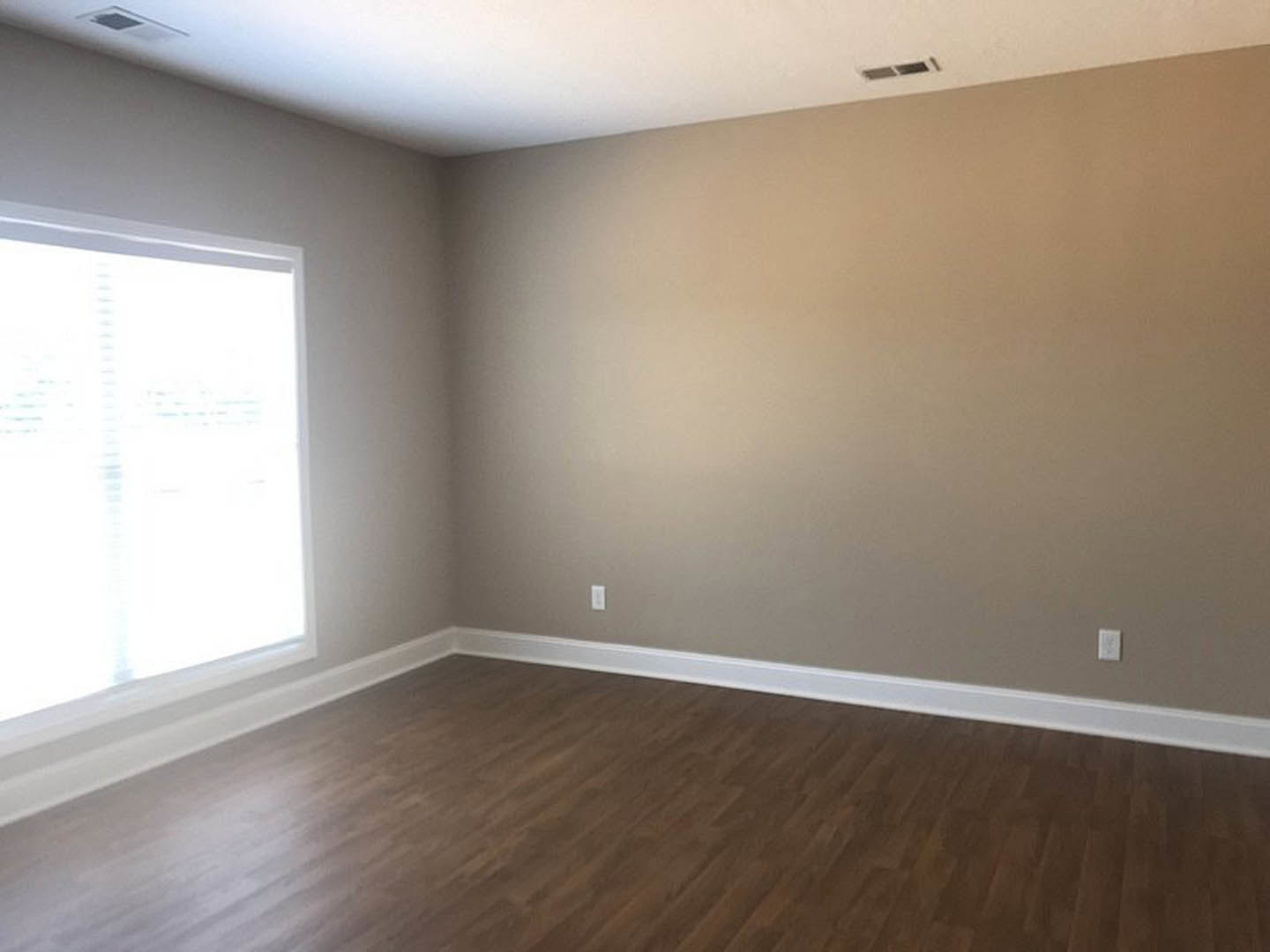 Room with white ceiling, brown accent wall, white-framed window, hardwood floor, and white baseboards
