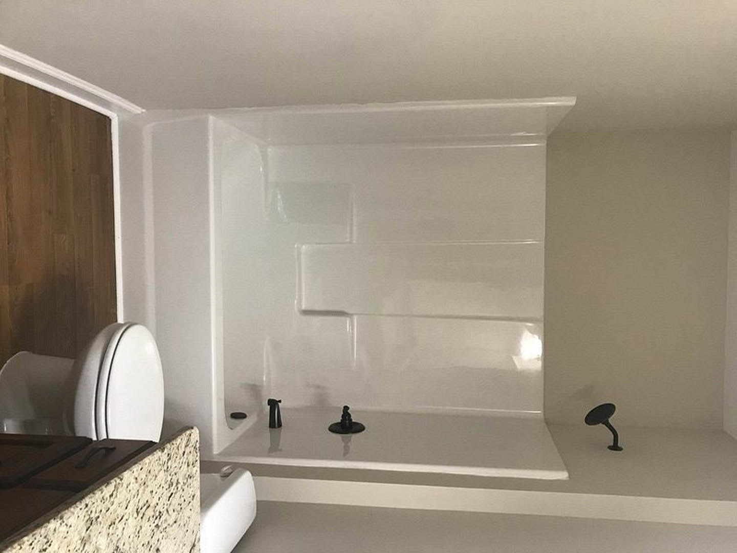 Freestanding white bathtub with matte black faucet, wood paneled vanity with black handles, white countertop, and plaster walls in modern bathroom