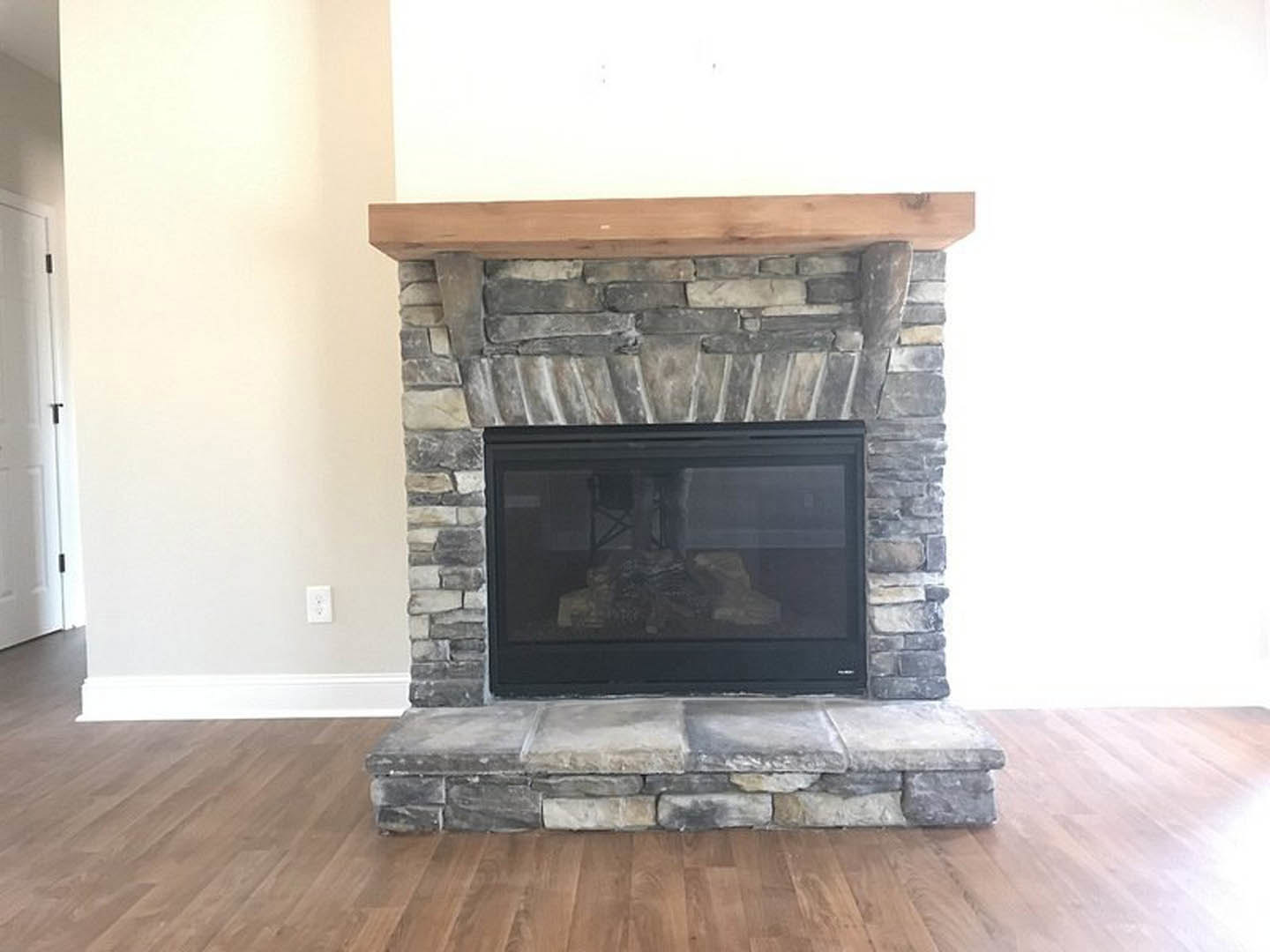 Stone fireplace with wood mantel, black fire screen, and wood flooring in a cozy indoor room; white door with black handle visible on the side.