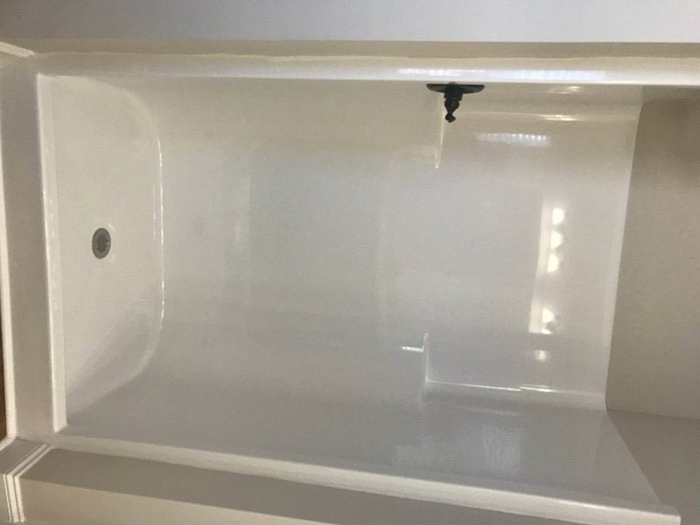 Freestanding white bathtub with chrome faucet set against smooth white plaster wall in modern master bathroom