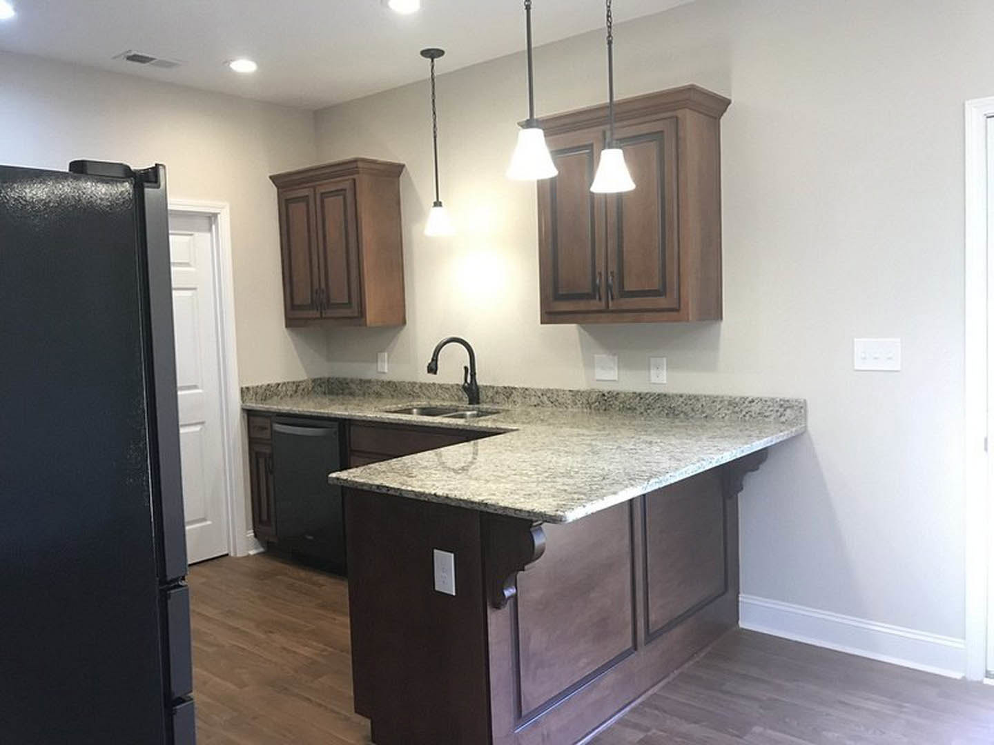 Granite countertop kitchen with white cabinetry, stainless steel sink, tile backsplash, and modern light fixture
