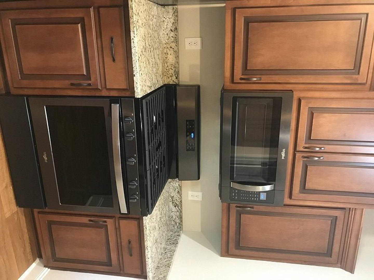 White shaker cabinets and drawers, stainless steel microwave oven built into cabinetry, black oven below, light wood flooring, glass pantry door, quartz countertop, wall outlet