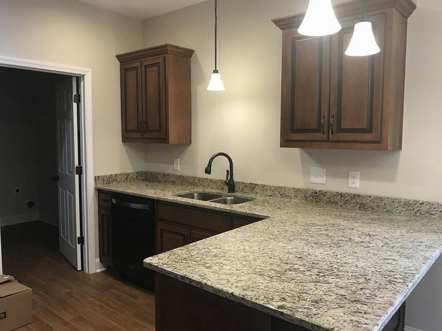 Granite countertops with undermount sink and black faucet, white cabinetry, tile backsplash, pendant light fixture, and a white wall accent in a custom kitchen