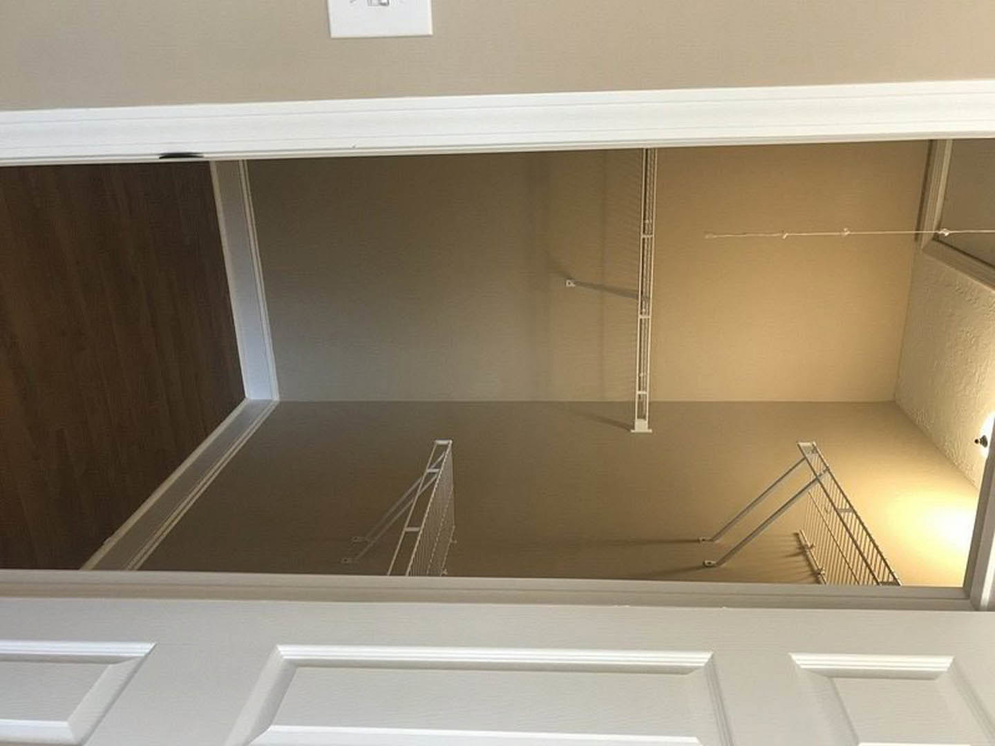 White paneled door open to a bright room with plaster walls, light wood flooring, and a staircase visible in the background.