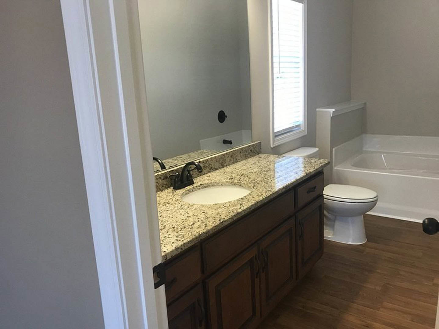 Modern bathroom with white porcelain sink and toilet, brown wood countertop, tile flooring, wall-mounted mirror, and a window providing natural light.