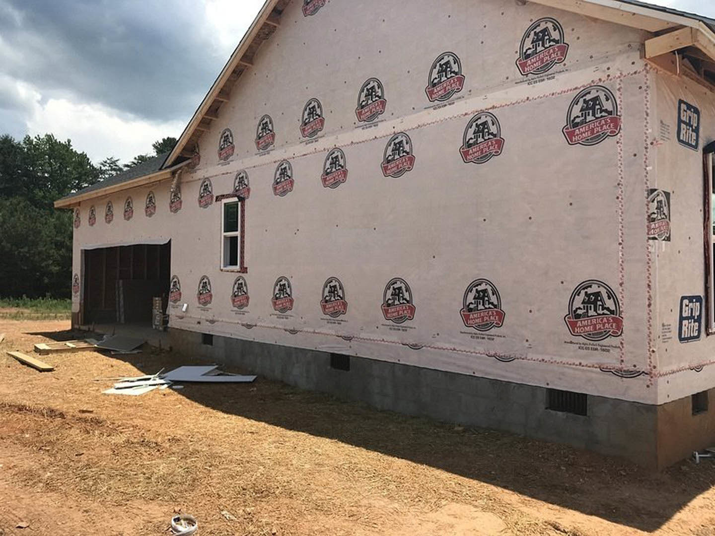 White stucco house exterior with red and black logo sign, white-framed windows, dark front door, and landscaping with trees under a cloudy sky