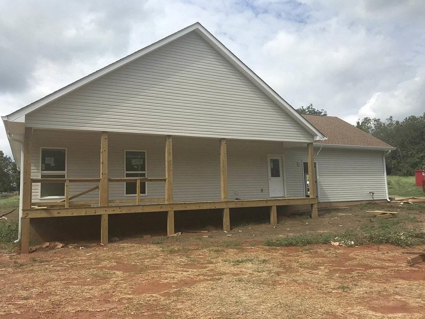 White cottage-style home with covered front porch, gray siding, gabled roof, and grassy yard; door features a window, and a large window displays a sign.