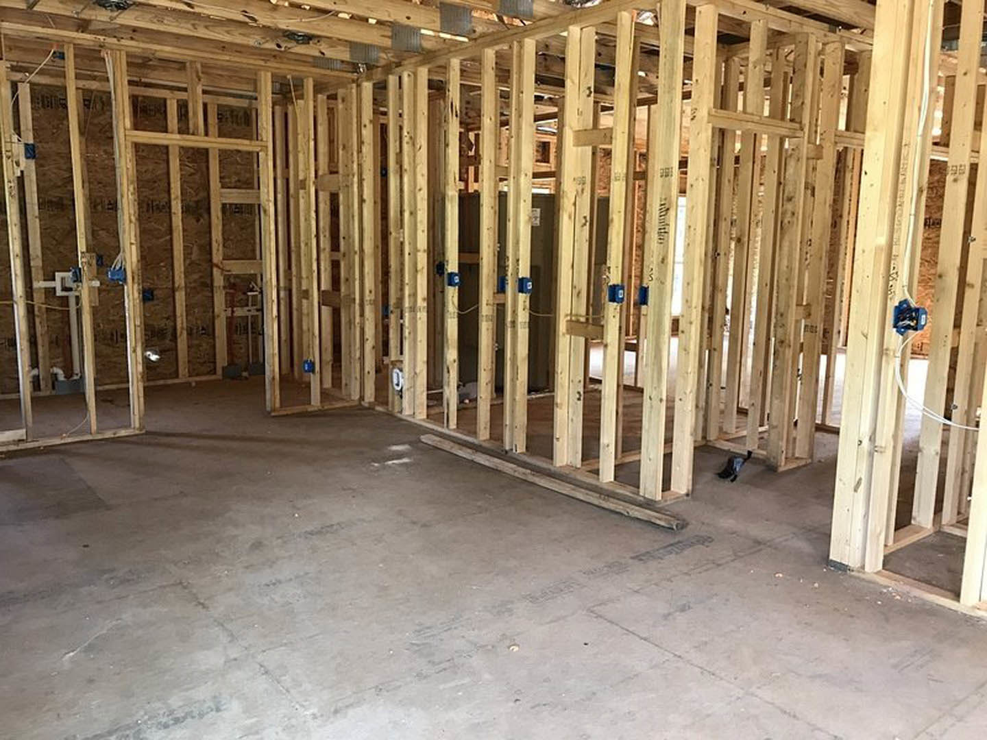 Wood-framed room under construction with exposed beams, concrete floor, black boot near wall, and insulation visible between studs