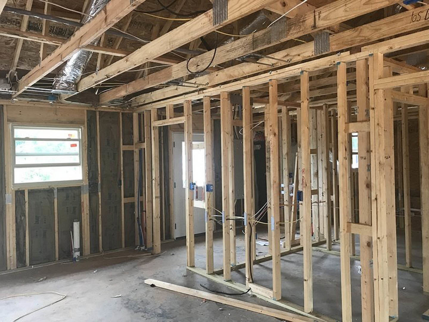 Wood-framed room under construction with exposed beams, wiring, and a white door featuring a window