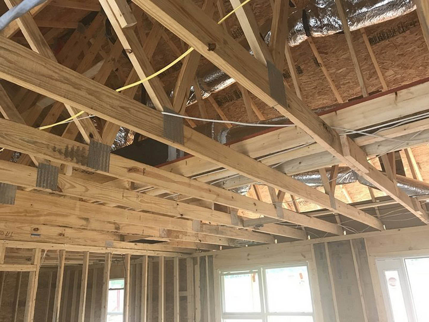 Exposed wooden ceiling beams above a bright interior with a white door featuring a glass window, adjacent to a large window and light-colored walls.