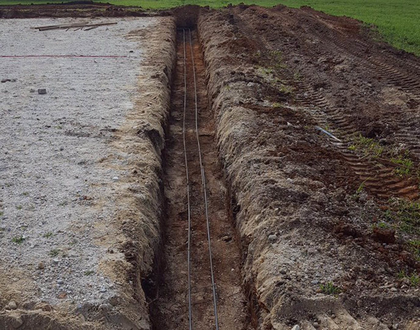 Narrow dirt trench running through grassy yard with exposed electrical wires laid in soil