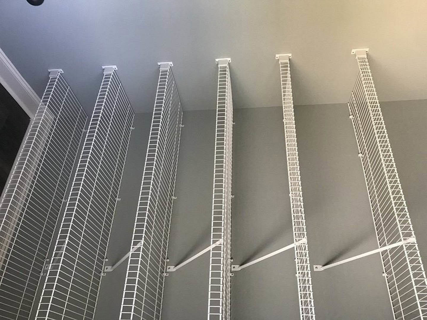 White metal shelving unit mounted on a light gray wall, featuring grid-like shelves and minimalist design in a modern interior space.