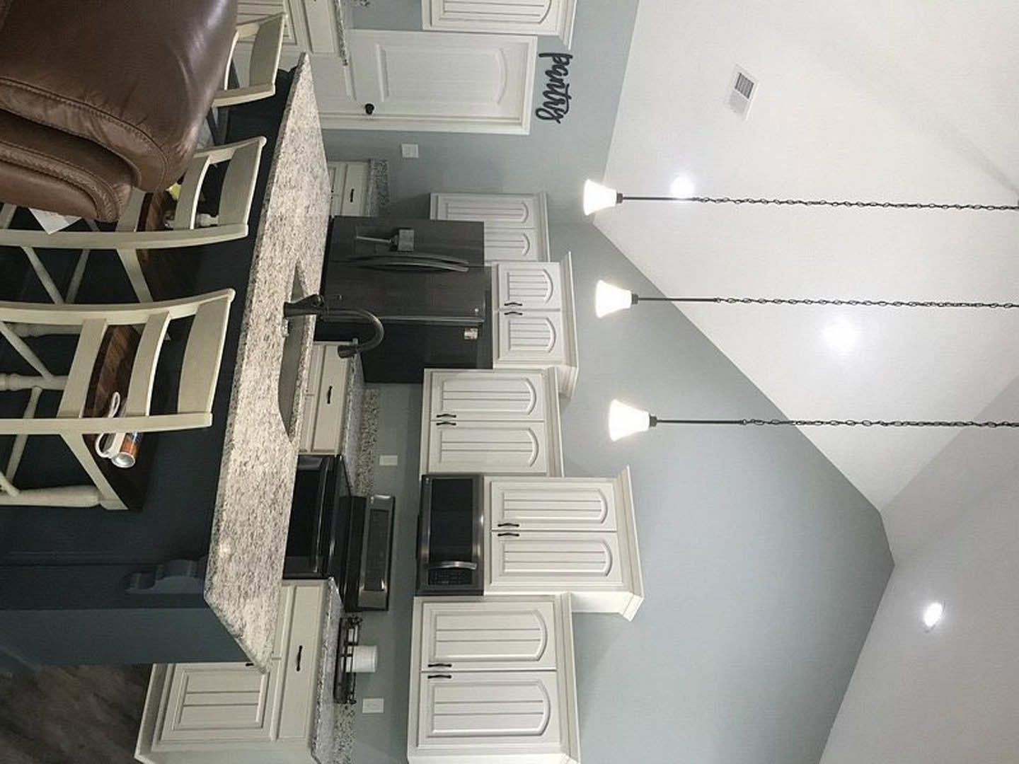 White kitchen cabinets with black refrigerator, white vent on wall, leather chair, white door with black handles, and white chair with decorative accent