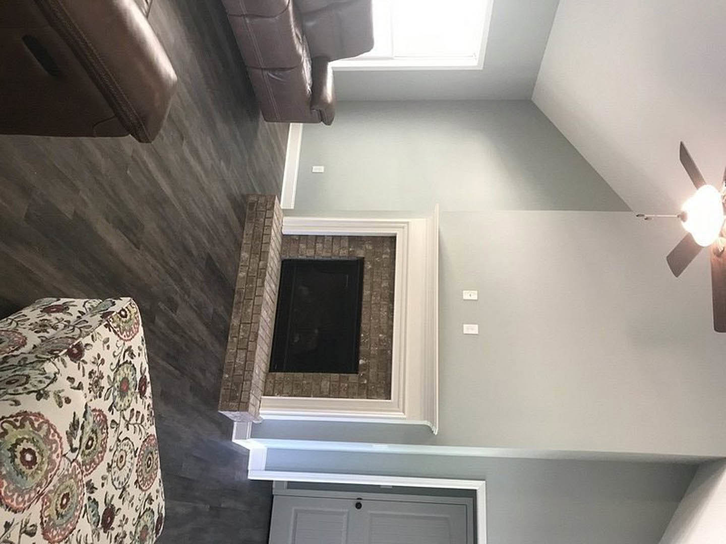Living room with light plaster walls, brick fireplace, rectangular window, gray upholstered couch, white molding, and wooden cabinetry