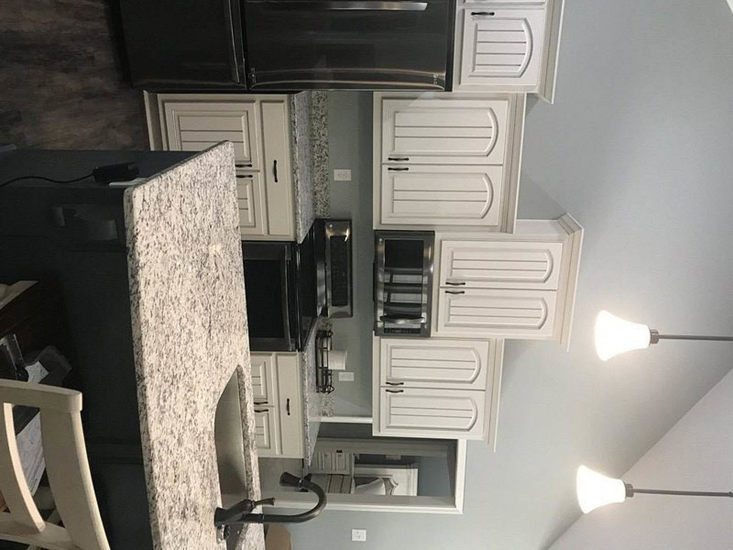 Granite kitchen countertops with black microwave, white cabinetry featuring black handles, staircase detail, white chair leg, and white chair beside marble fireplace