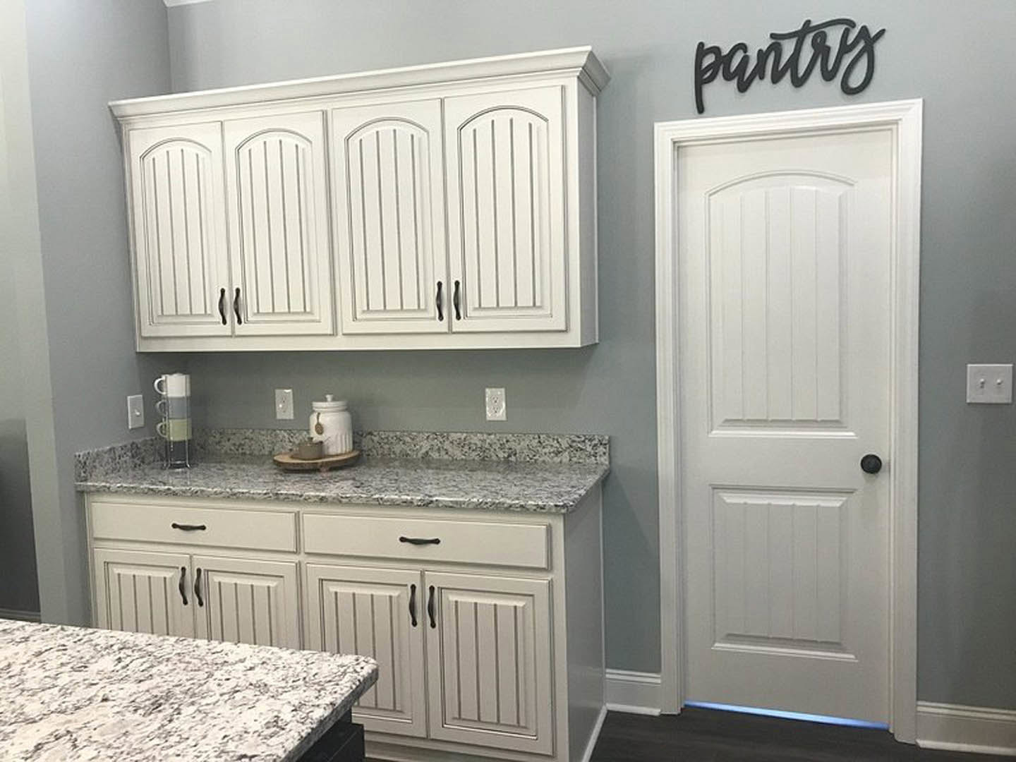 White kitchen cabinets with black handles, granite countertops, stainless steel sink, and a white jar with lid on the counter