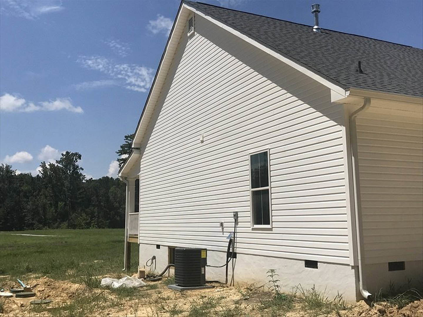 Modern two-story home with light siding, expansive grassy yard, black rainwater tank beside the house, large windows, brick chimney, and mature trees bordering the property.